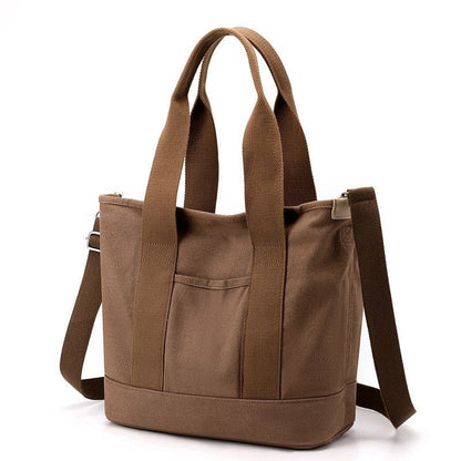 The large brown tote bag with zipper is made of canvas material, being able to be carried on the shoulder or crossbody.